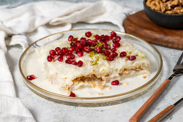 Gullac dessert. Ramadan dessert. Gullac garnished with pomegranate and pistachio in glass plate on gray background. Symbolic food.
