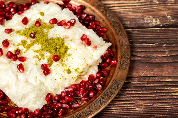 Gullac dessert. Ramadan dessert. Gullac decorated with pomegranate and pistachio on a copper plate on wood background. Symbolic food.