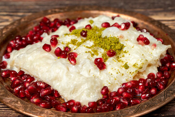 Gullac dessert. Ramadan dessert. Gullac decorated with pomegranate and pistachio on a copper plate on wood background. Symbolic food.