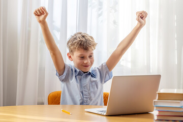 Excited schoolboy learning online on laptop