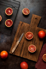 Red oranges on a wooden cutting board, dark background. Top view, flat lay, vertical