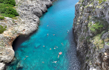 view from above on the turquoise water and swimmers in a bay of the Adriatic in Puglia bordered by cliffs