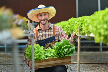 Smiling caucasian farmer in apron harvesting organic vegetables standing in greenhouse. Business agriculture concept