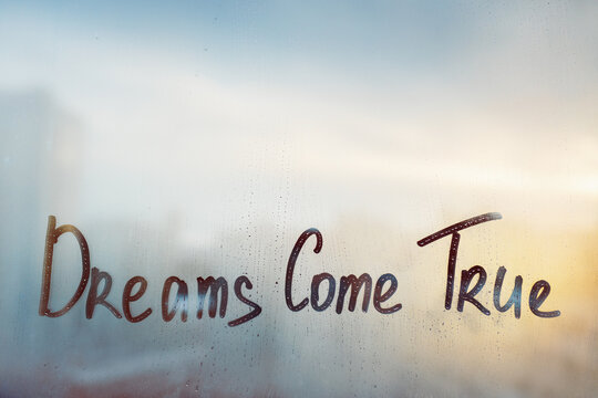 Dreams come true message written finger on foggy glass wet sunset window