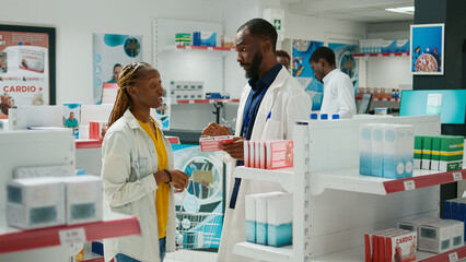 Obraz premium Male doctor recommending healthcare products to client, showing medicaments and supplements to cure disease. Young woman talking to specialist about treatment, buying box of pills.