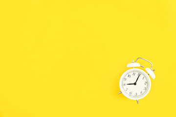 White alarm clock on a yellow background, flat lay.
