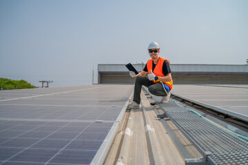 Asian engineer wearing protective vest and white hardhat sitting thumb ups while holding tablet with smile on solar panels roof, Photovoltaic technology concept.