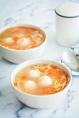 Potato balls soup with noodles and vegetables in white bowl, white background. Vegan food concept.