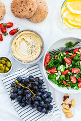Vegan picnic food: hummus, lemonade, broccoli salad and fruits on white blanket on the grass.