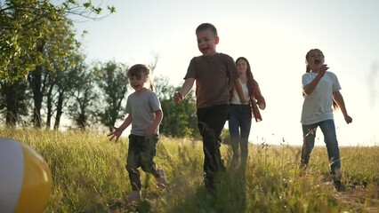 Teamwork. Group of children in spring in park on green grass with ball. Family playing football on the green grass. Children summer vacation in park. Schoolchildren play with ball in meadow in grass.