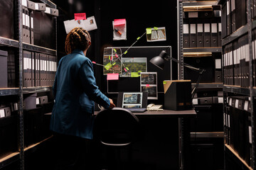 Woman looking at detective board and analyzing crime case evidences. African american woman police...