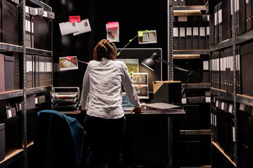 Woman private detective studying crime case board hanging on wall. African american police...