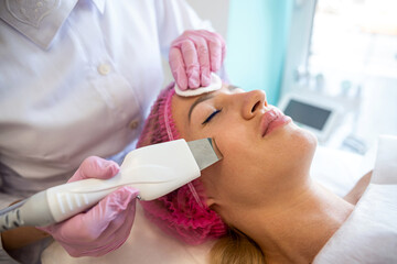 beautician with an ultrasonic scrubber works with the skin of a woman's face.