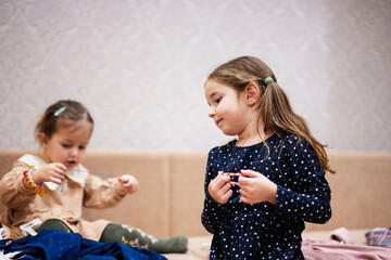 Two sisters are choosing clothes from the wardrobe at home on the sofa. Girl chooses a bracelet for her hand.