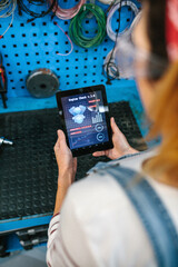 Unrecognizable mechanic woman checking a engine diagnosis app in digital tablet over garage workbench
