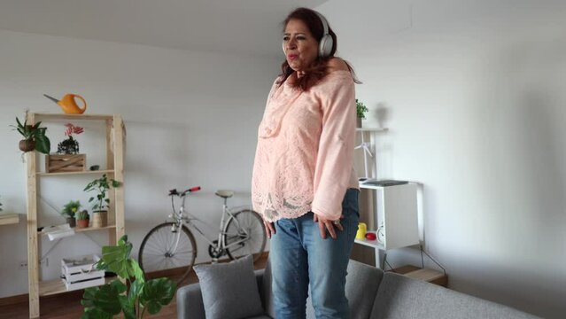 curvy mature woman listen music and dance on sofa at home happy