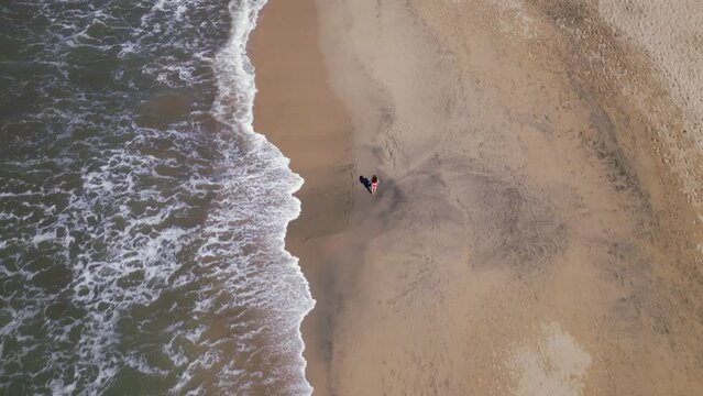 A Woman Walks Along A Beach As Seen From An Overhead Aerial Drone