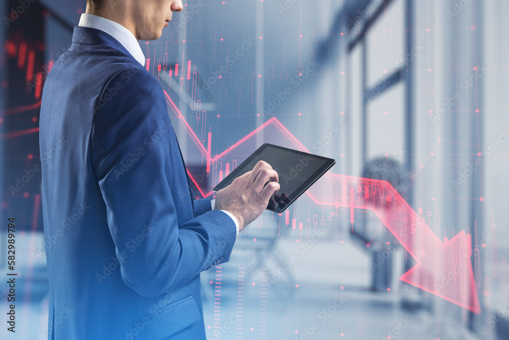 Poster close up of businessman hands using tablet with red candlestick arrow going down on blurry office in