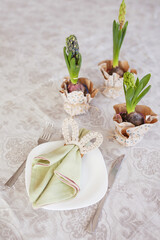 Spring festive dining table setting with flowers, napkins and cute bunny decor on linen tablecloth. Easter time. Cozy home