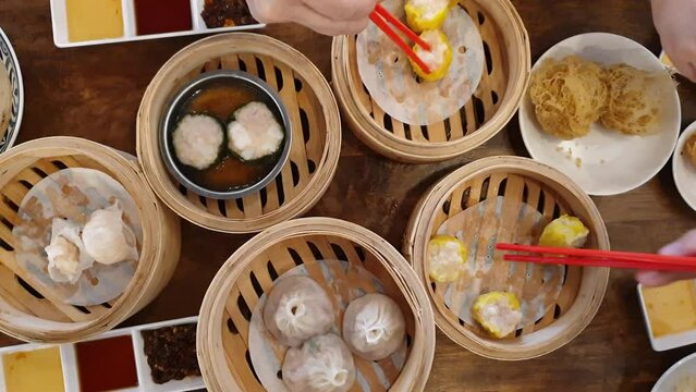 Hands chopsticks eating dim sum shu mai Chinese hong kong style breakfast food steamed dumplings stuffed bao