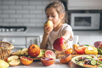 Funny little girl eating apples in the kitchen, health and nutrition concept.