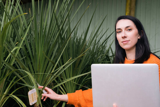 Woman with laptop putting labels on plants in garden center
