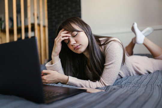 Tired young woman with eyes closed lying on bed at home