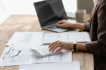 Fototapeta premium Close-up shot of businesswoman using calculator and laptop to calculate company financial result On wooden table in office and business background, tax, accounting, statistics and analytical research.
