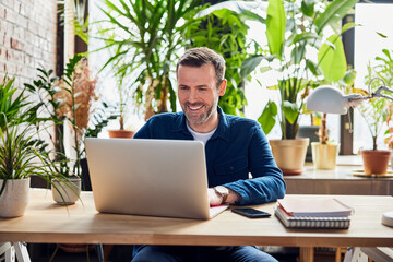Happy businessman working on laptop at loft office