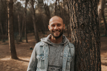 Happy man leaning on tree trunk in forest