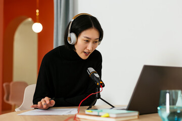 Woman wearing headphones talking on microphone in podcast studio