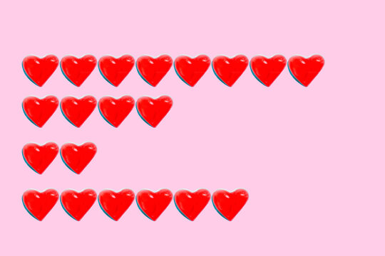 Rows of heart shaped candy flat laid against pink background