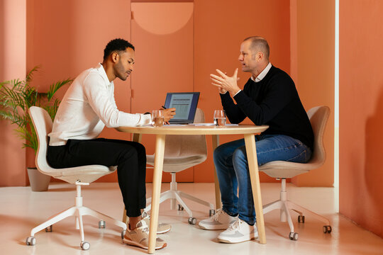 Businessman discussing with colleague at desk in front of orange wall