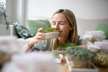 Woman with eyes closed smelling herbs at home