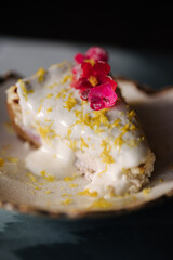 A piece of cheesecake with sweet cream sauce and lemon zest, decorated with an edible pink flower