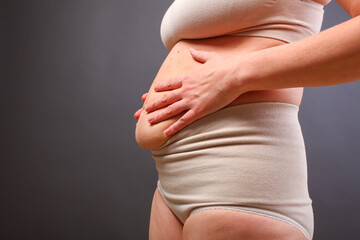 young woman in postpartum corrective tightening underwear shows her overweight. The girl squeezes her excess belly fat with her hands after childbirth