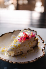 A piece of cheesecake with sweet cream sauce and lemon zest, decorated with an edible pink flower