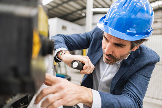 Engineer holding torch analyzing machine part in factory