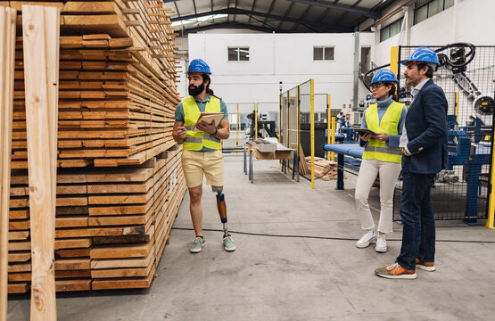 Engineer examining stack of planks with colleagues in factory