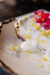 A piece of cheesecake with sweet cream sauce and lemon zest, decorated with an edible pink flower