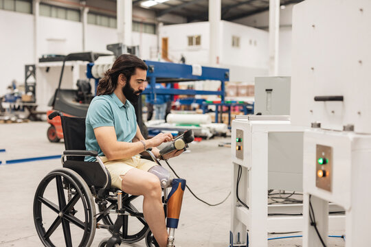 Engineer sitting in wheelchair using controller of machine in industry