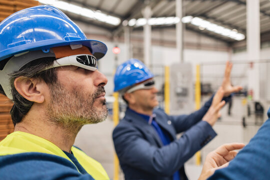 Mature engineer wearing smart glasses standing by colleague in factory