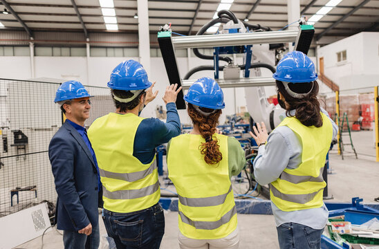 Engineers wearing hardhat examining machine part in robotics factory