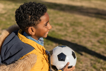 Happy boy wearing parka coat holding soccer ball in park