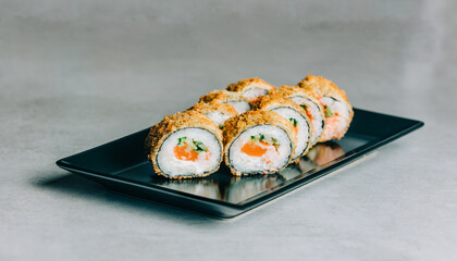 Warm sushi rolls in dried breadcrumbs with salmon on black plate on gray background