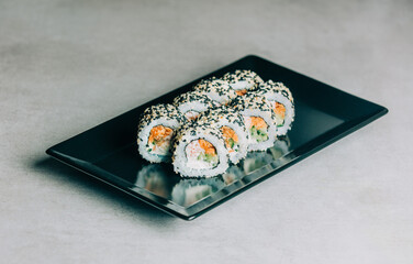 sushi rolls in sesame with salmon on black plate on gray background