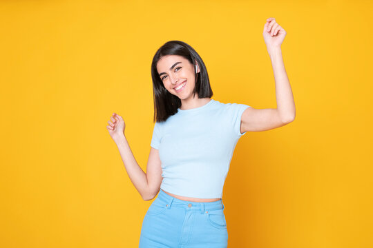 Happy Young Woman Dancing Against Yellow Background