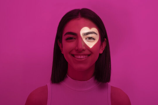 Smiling woman with heart shaped light on eye against pink background