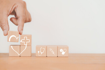 For health insurance, wellness, wellbeing concept, hand hold part of heart icon on wooden cube blocks  with other medical sign including copy space