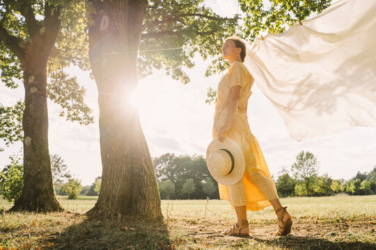 Thoughtful woman standing with hat at park